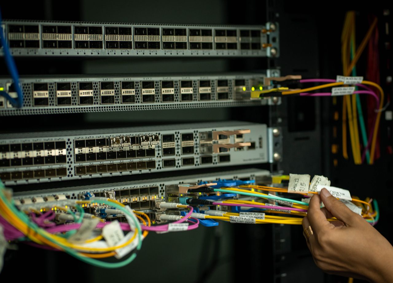 services-03 A hand managing fiber optic cables in a server room, showcasing modern connectivity.
